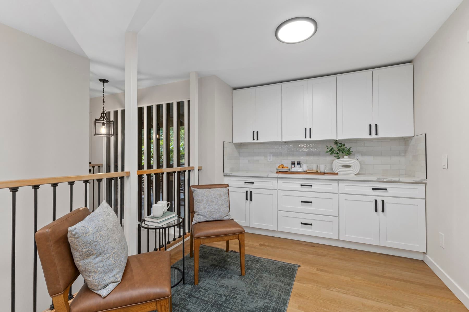 The finished kitchen, white cabinetry and a staged breakfast chair beside the stair rail.