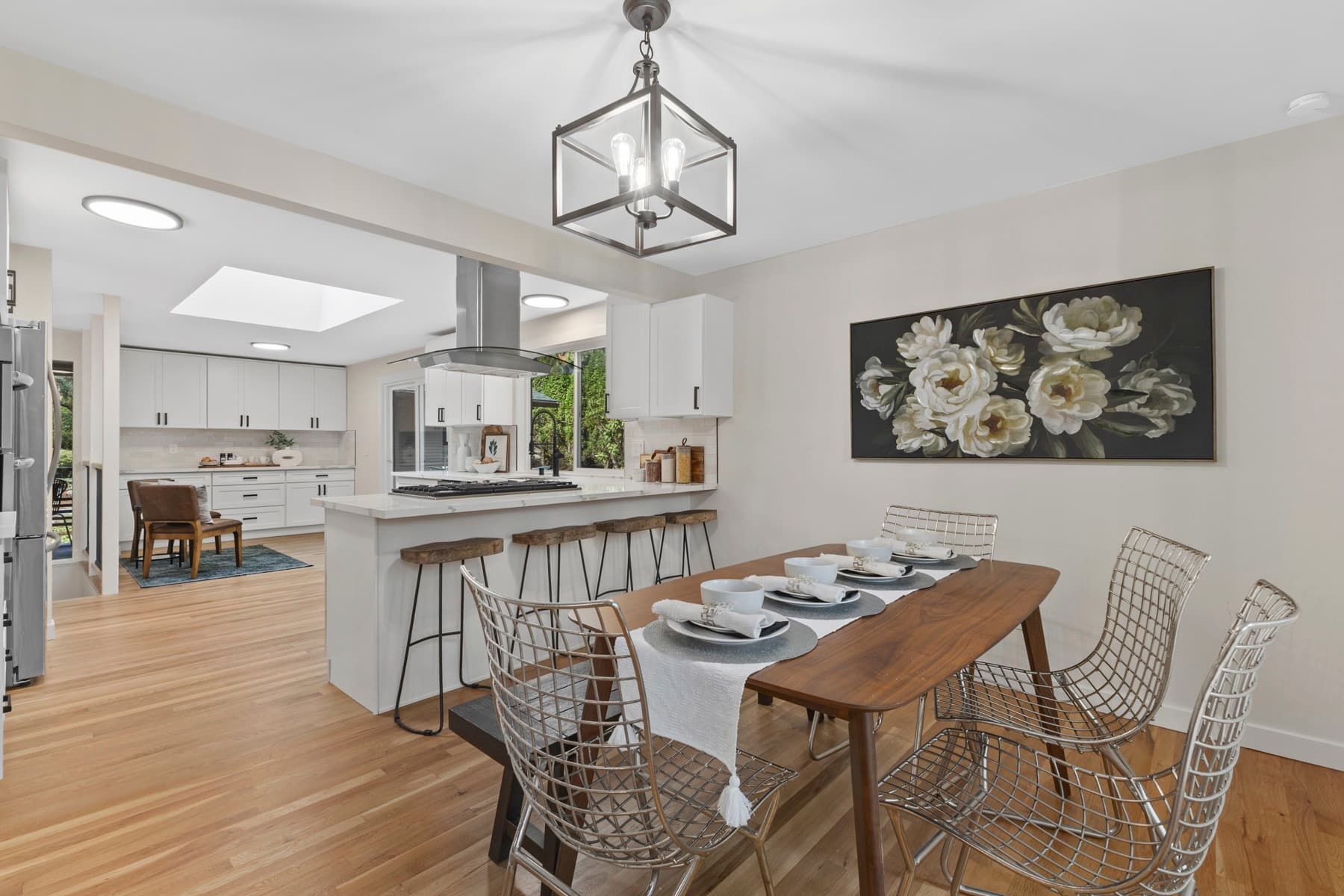 The staged dining room under a lantern pendant, the finished kitchen and its island beyond.