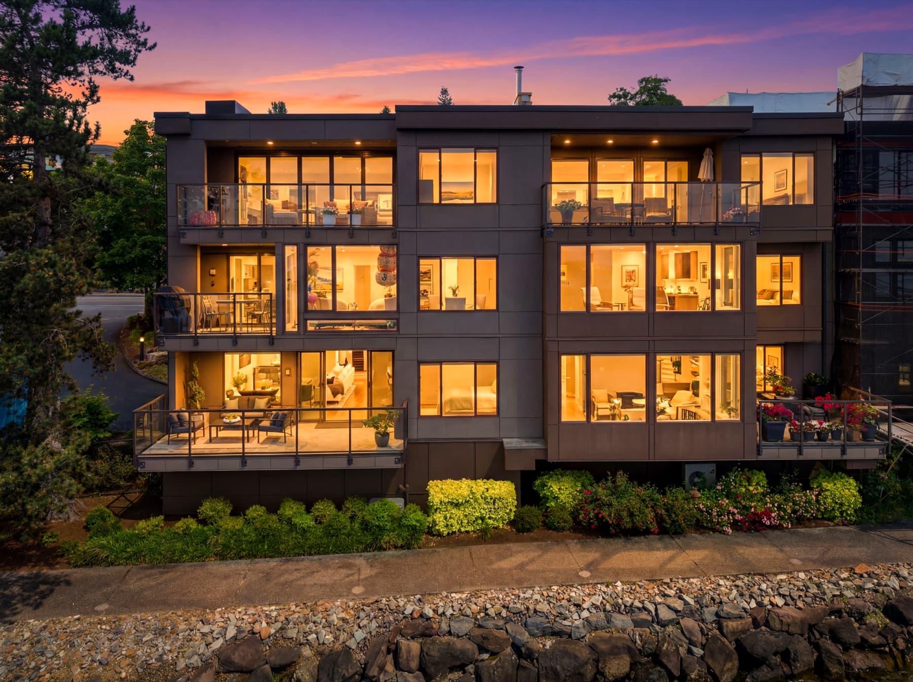 The condominium building seen from the shoreline at dusk, its windows lit and the water in the foreground.