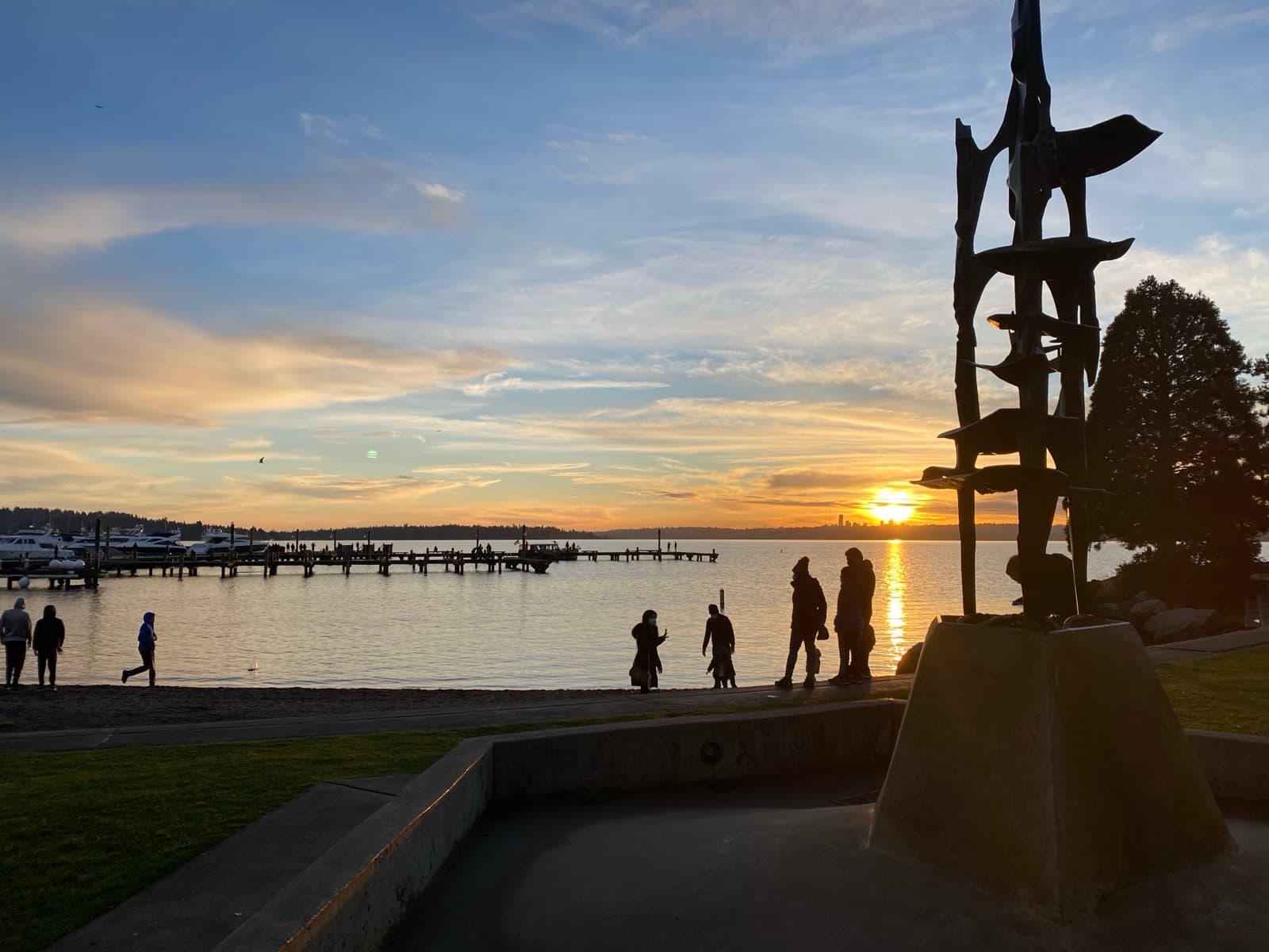 Sunset over Marina Park in Kirkland, with the public pier, a marina, and people gathered on the shore.