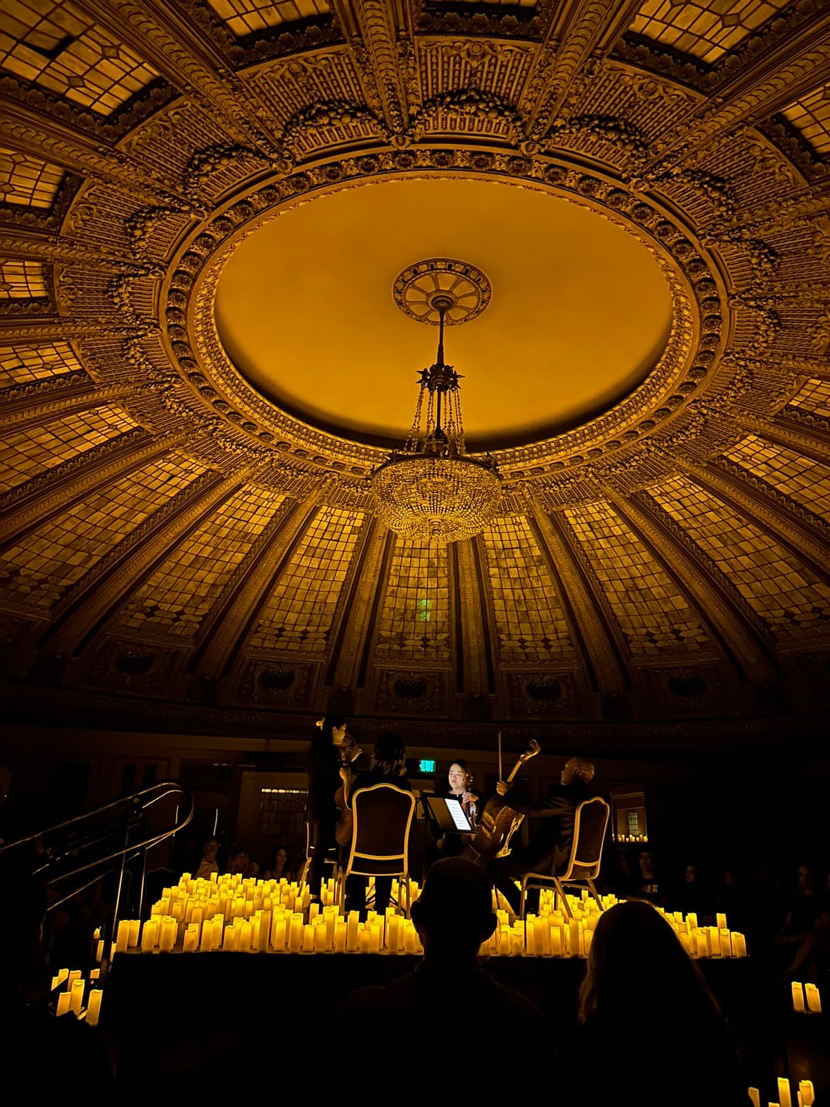 The gilded dome, chandelier and stained glass ceiling of the Arctic Club Hotel’s Dome Room in Seattle, with musicians performing among rows of lit candles.