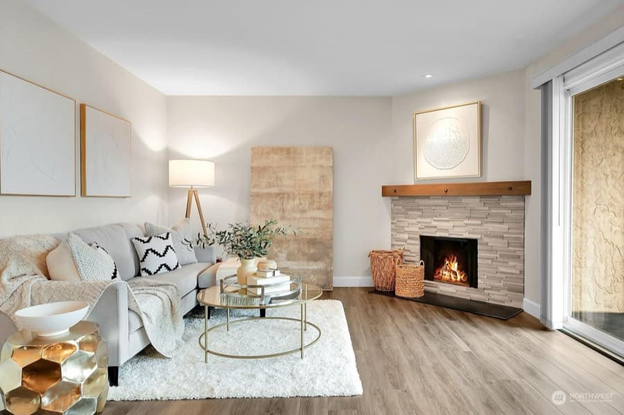 A staged living room: a stone fireplace, a pale sofa with cushions, a round coffee table on a light rug.